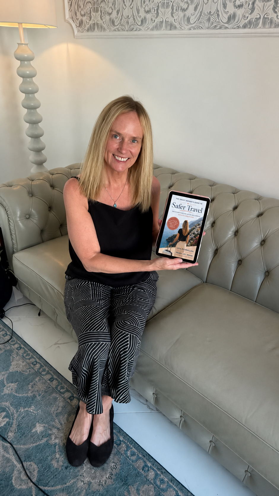 Lisa, author of The Smart Woman's Guide to Safer Travel, holding a tablet showing the book cover